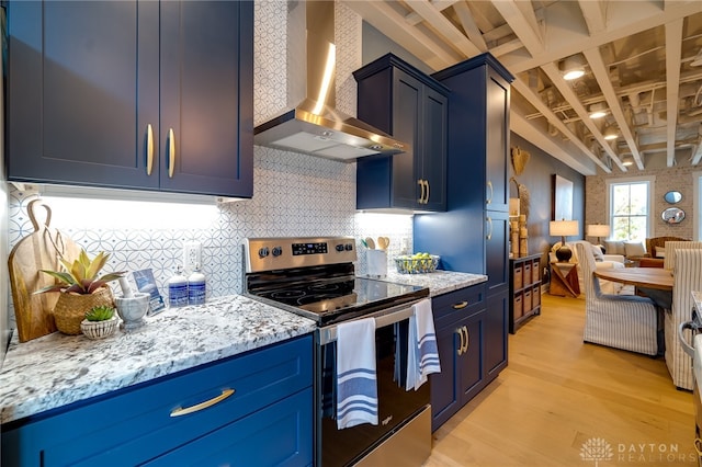 kitchen with light wood-type flooring, stainless steel range with electric stovetop, blue cabinets, wall chimney exhaust hood, and light stone counters