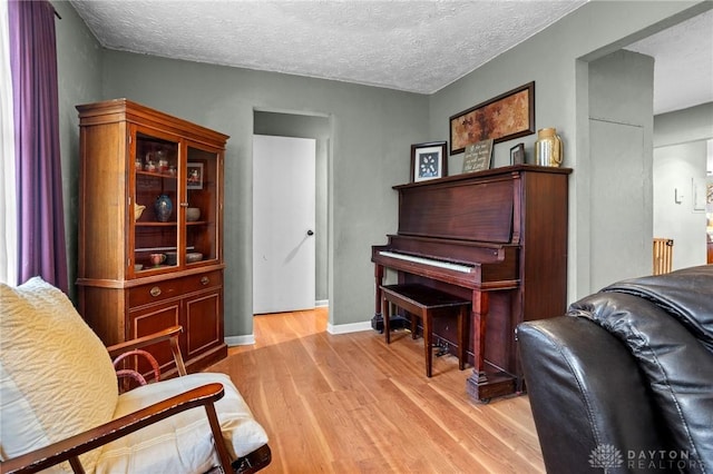 sitting room with light wood-type flooring, baseboards, and a textured ceiling