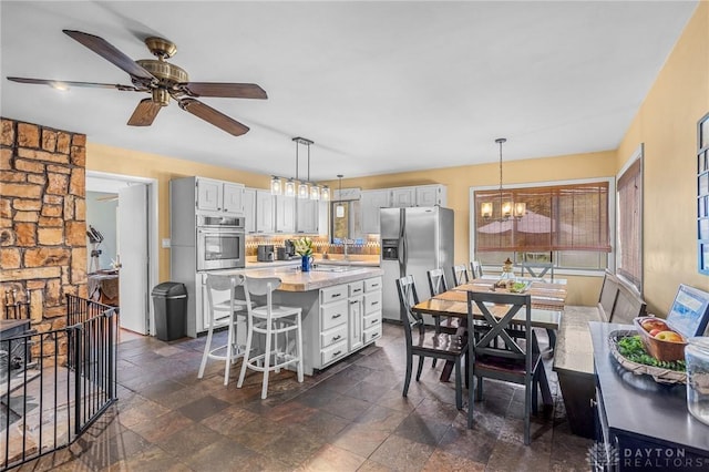 kitchen featuring a healthy amount of sunlight, an inviting chandelier, stainless steel fridge, stone finish flooring, and tasteful backsplash