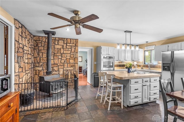 kitchen with a breakfast bar, a wood stove, stainless steel appliances, light countertops, and a center island