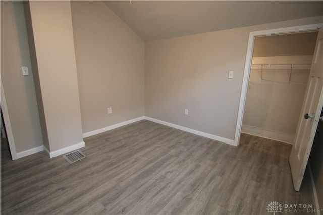 unfurnished bedroom featuring a spacious closet, a closet, vaulted ceiling, and hardwood / wood-style floors