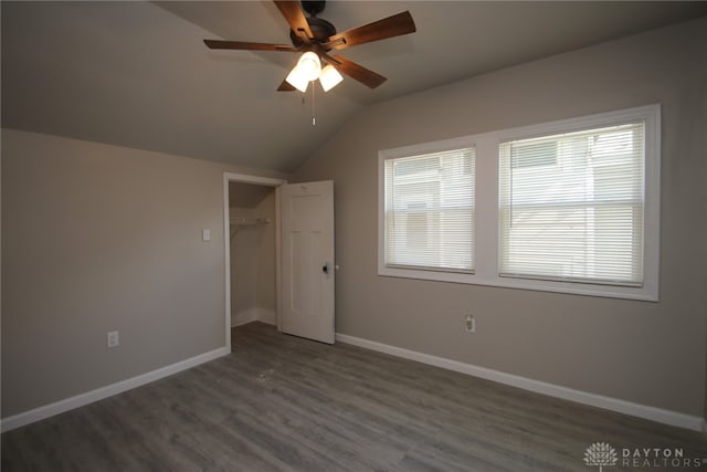 unfurnished bedroom with a spacious closet, a closet, ceiling fan, vaulted ceiling, and dark wood-type flooring