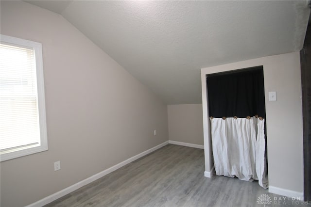 bonus room with a textured ceiling, light wood-type flooring, and vaulted ceiling