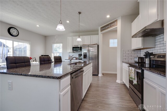 kitchen with dark stone counters, a center island with sink, white cabinets, sink, and stainless steel appliances