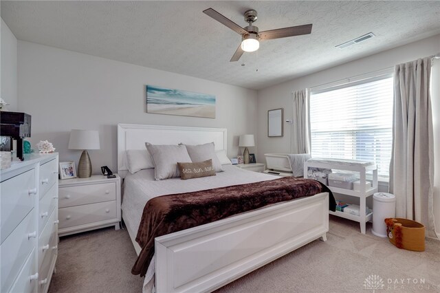 bedroom with ceiling fan, light colored carpet, and a textured ceiling