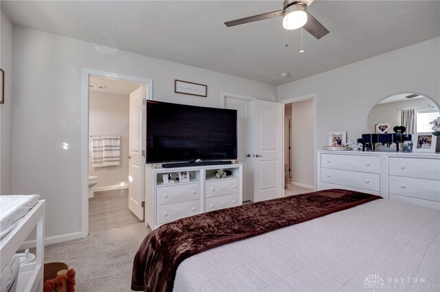 bedroom with ceiling fan, light colored carpet, and connected bathroom