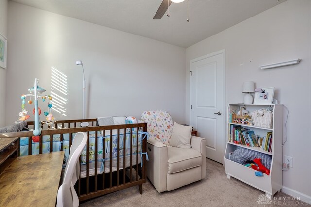 carpeted bedroom featuring ceiling fan and a nursery area