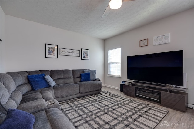 living area with ceiling fan, a textured ceiling, baseboards, and wood finished floors