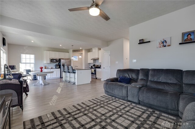 living room with ceiling fan, light wood-type flooring, and a textured ceiling