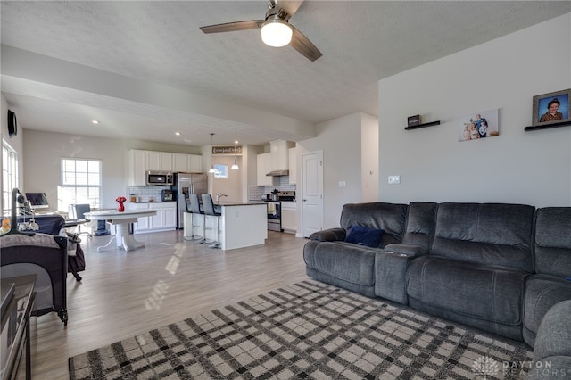 living room with a ceiling fan, light wood-style floors, and a textured ceiling