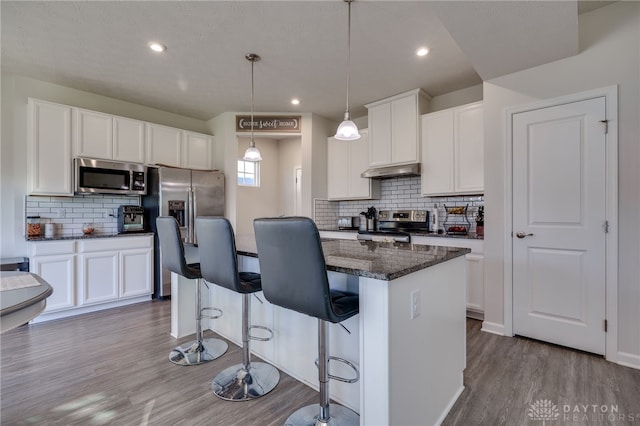 kitchen with wood finished floors, a kitchen island, stainless steel appliances, under cabinet range hood, and white cabinetry