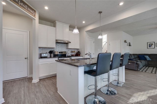 kitchen with under cabinet range hood, stainless steel range with electric stovetop, a kitchen breakfast bar, wood finished floors, and a sink