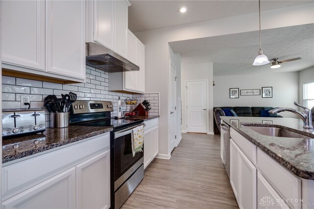 kitchen with appliances with stainless steel finishes, sink, dark stone countertops, white cabinetry, and hanging light fixtures