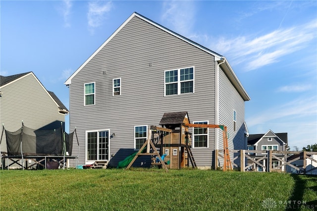 back of house with entry steps, a trampoline, fence, a playground, and a yard