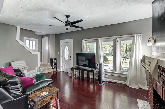 living room with ceiling fan, a fireplace, dark wood-type flooring, and a textured ceiling