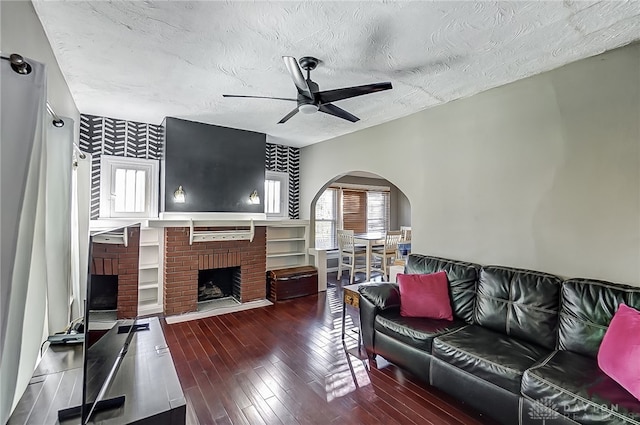 living room featuring a textured ceiling, dark hardwood / wood-style floors, a brick fireplace, and ceiling fan