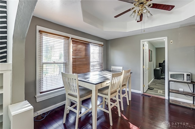 dining room featuring ceiling fan, dark hardwood / wood-style flooring, and a tray ceiling