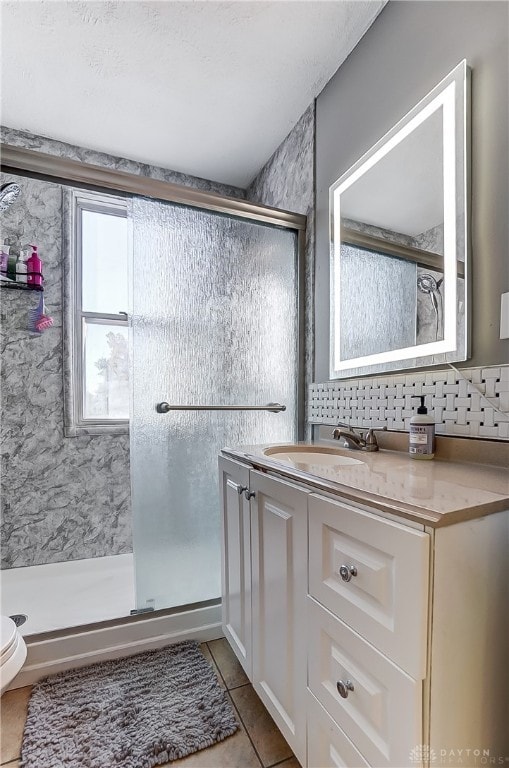 bathroom featuring tile patterned floors, backsplash, toilet, vanity, and a shower with shower door