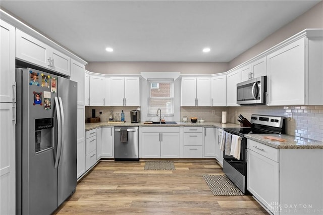 kitchen featuring appliances with stainless steel finishes, light wood-type flooring, light stone counters, sink, and white cabinets