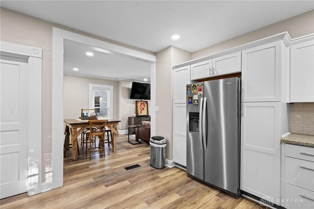 kitchen featuring light wood-type flooring, backsplash, light stone counters, stainless steel fridge with ice dispenser, and white cabinetry