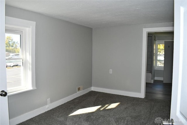 empty room with a healthy amount of sunlight, a textured ceiling, and dark carpet