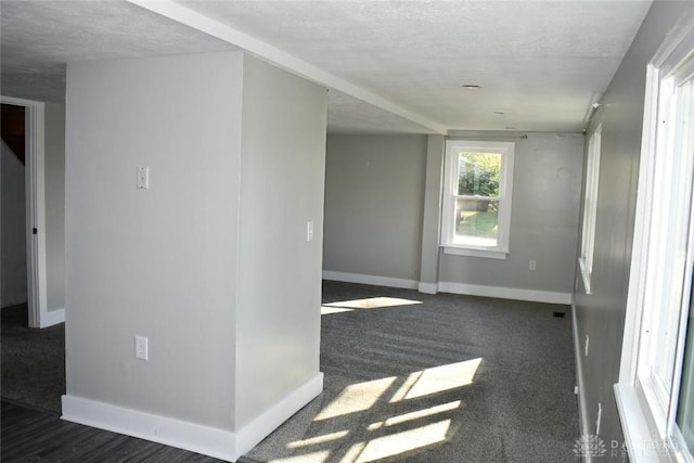 empty room featuring a textured ceiling, dark carpet, and a healthy amount of sunlight