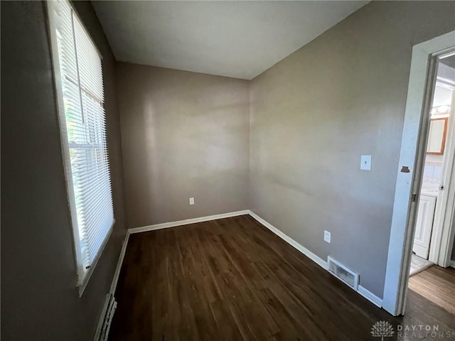 empty room with a baseboard heating unit and dark hardwood / wood-style floors