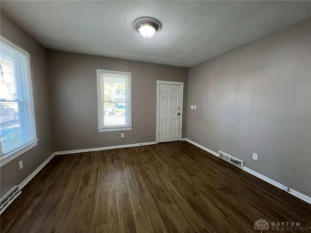 empty room with a baseboard heating unit, dark wood-type flooring, and a textured ceiling