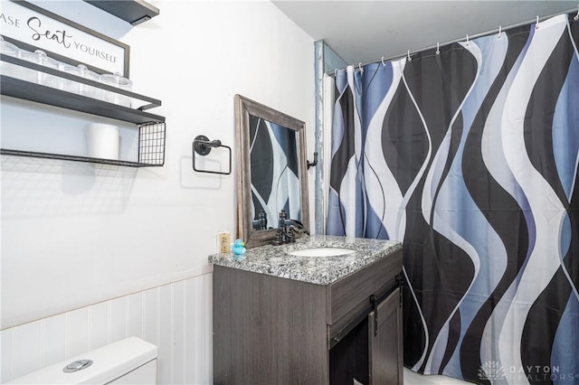 bathroom featuring toilet, a wainscoted wall, a shower with curtain, and vanity