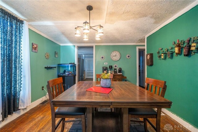 dining space with hardwood / wood-style flooring, a chandelier, a textured ceiling, and ornamental molding