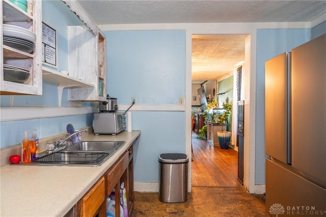 kitchen with fridge, a textured ceiling, light countertops, and a sink