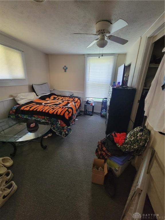 bedroom with ceiling fan, dark carpet, and a textured ceiling