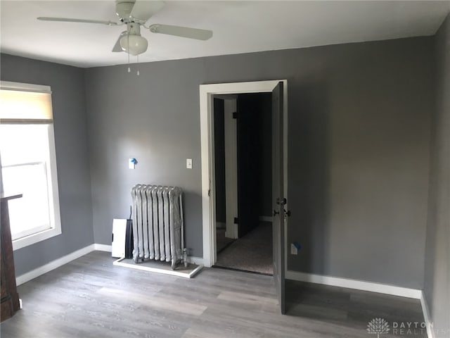 unfurnished room with radiator, a ceiling fan, baseboards, and wood finished floors