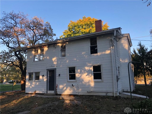 rear view of property with a chimney and fence