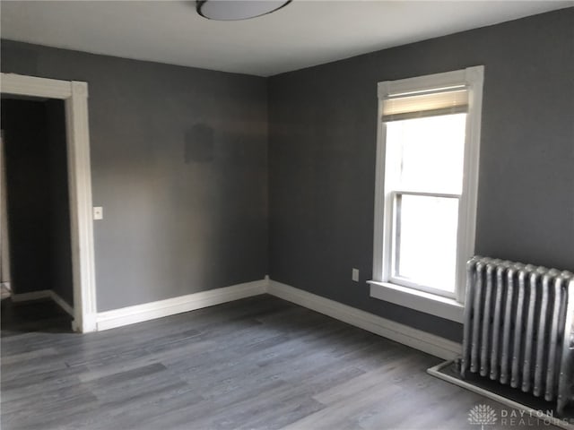 unfurnished room with radiator, baseboards, and wood finished floors