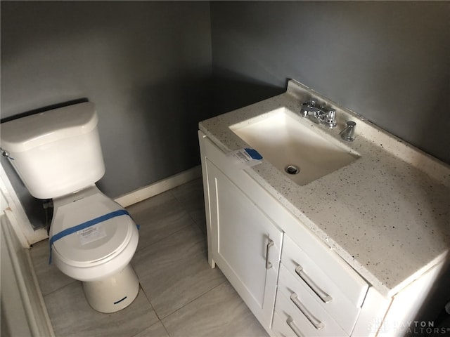 half bathroom with baseboards, vanity, toilet, and tile patterned floors