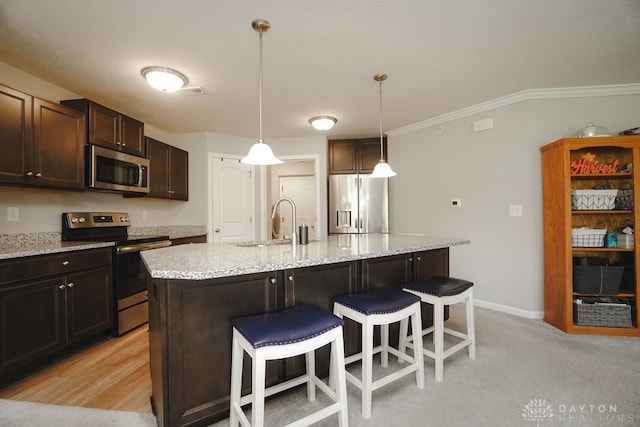 kitchen with ornamental molding, dark brown cabinets, stainless steel appliances, pendant lighting, and a center island with sink