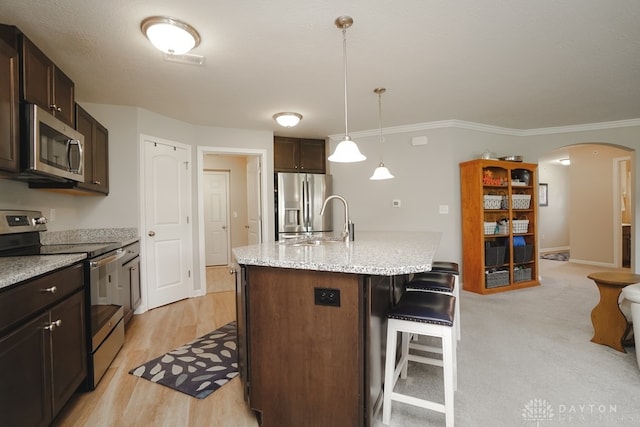 kitchen featuring sink, a kitchen breakfast bar, an island with sink, appliances with stainless steel finishes, and light wood-type flooring