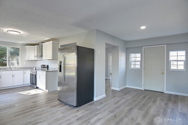 kitchen featuring wall chimney range hood, appliances with stainless steel finishes, white cabinetry, light wood-type flooring, and light stone counters