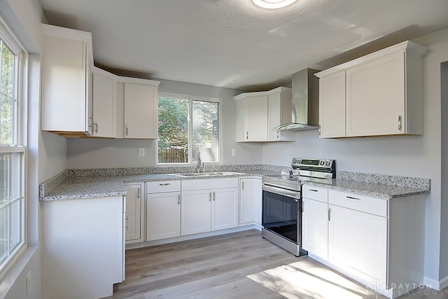 kitchen featuring sink, white cabinetry, wall chimney exhaust hood, stainless steel electric range, and light hardwood / wood-style flooring