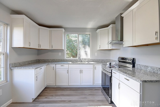 kitchen with sink, stainless steel electric stove, white cabinetry, wall chimney exhaust hood, and light hardwood / wood-style flooring