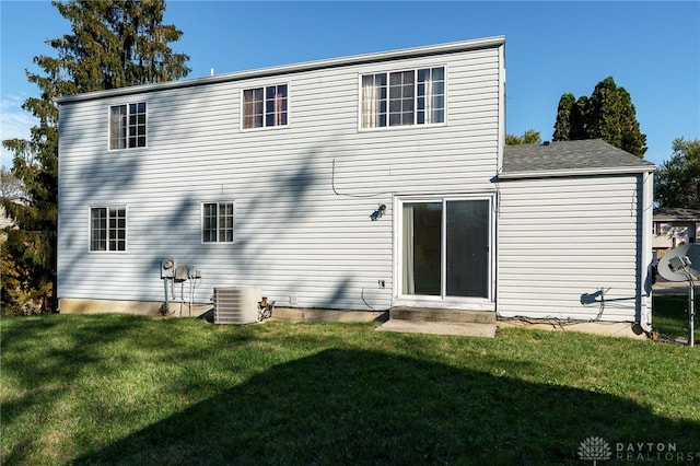 rear view of house with central AC unit and a lawn