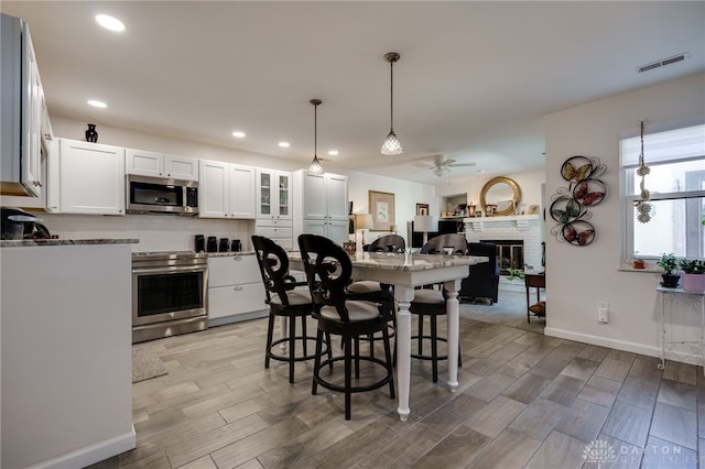 kitchen with white cabinets, ceiling fan, a fireplace, decorative light fixtures, and stainless steel appliances