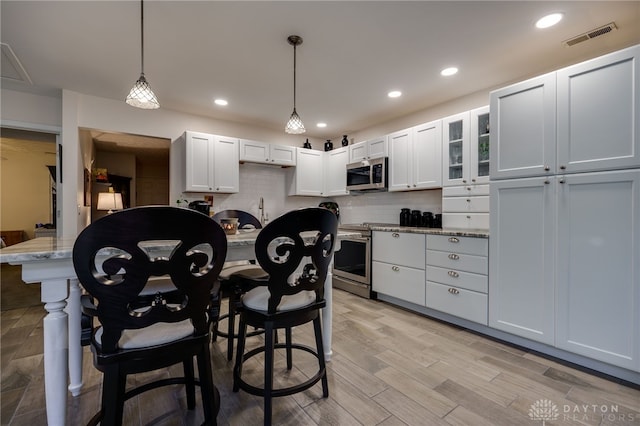 kitchen with light stone counters, white cabinetry, hanging light fixtures, and stainless steel appliances