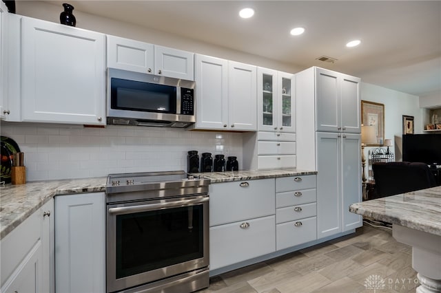 kitchen with appliances with stainless steel finishes, white cabinetry, light stone countertops, and tasteful backsplash