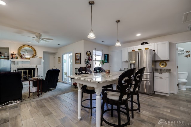 dining room with ceiling fan, wood-type flooring, and a brick fireplace