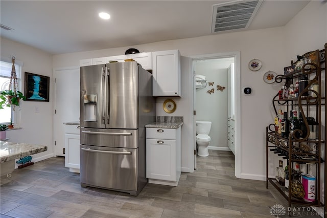 kitchen with white cabinetry, light stone countertops, and stainless steel fridge