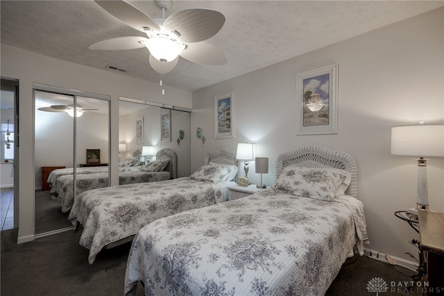 bedroom with a textured ceiling, two closets, carpet floors, and ceiling fan