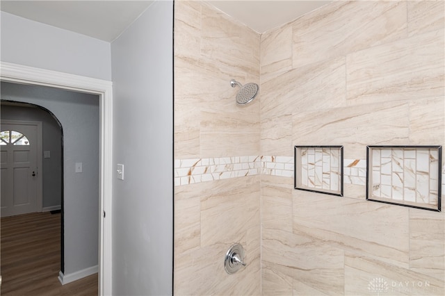 bathroom with a tile shower and wood-type flooring