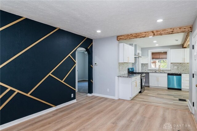 kitchen with appliances with stainless steel finishes, backsplash, white cabinetry, beamed ceiling, and light hardwood / wood-style flooring